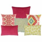 Three multi patterned cushion in fuchsia and yellow colours. Two cushion with diamond and leaf designs. One plain fuchsia cushion, one fur yellow cushion and one plain rectangular cushion in fuchsia colour.