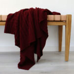 An image of a burgundy knitted throw draped over a stool
