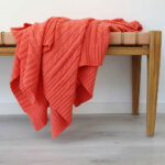 An image of a coral knitted throw draped over a stool