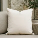Cream outdoor cushion in soft beige on fabric sofa with neutral backdrop.
