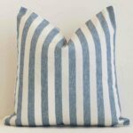 Blue stripe cushion cover in front of a white wall. It has a square size and is made from a outdoor material.