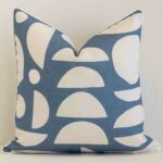 Bold square blue cushion positioned in front of white brickwork. Its geometric style pops on the outdoor fabric.