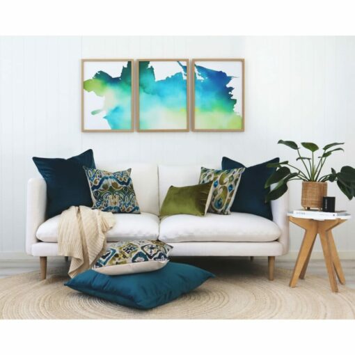 Olive and teal cushions and wall art in Ikat pattern against a white wall and sofa.