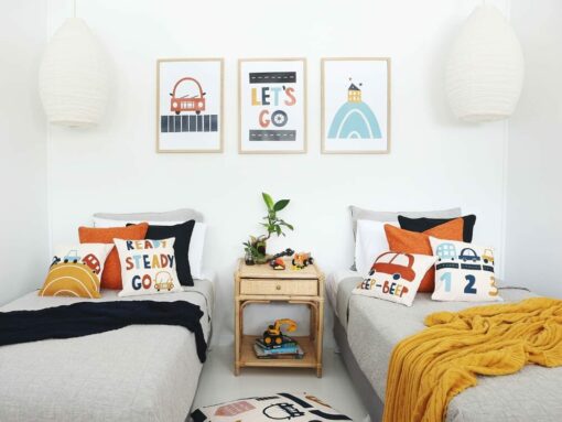 Kids bedroom with car kids cushions on twin beds with a throw blanket. On the wall are three kids wall prints that match the cushions