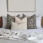 A bed with a wooden headboard adorned with the Nellie bed set showcasing four designer cushions.