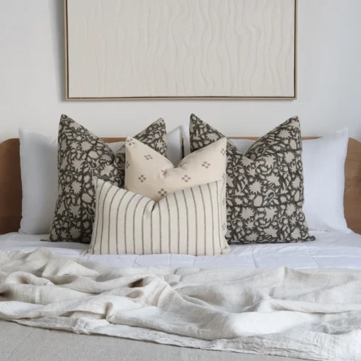 A bed with a wooden headboard adorned with the Nellie bed set showcasing four designer cushions.