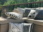 An outdoor setting is shown with a bold collection of black and white outdoor cushions adorning an outdoor sofa. The covers have striped and other markings which provide a tribal aesthetic.