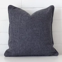 Here a charcoal linen cushion is shown styled against a white wall. It has a square design.