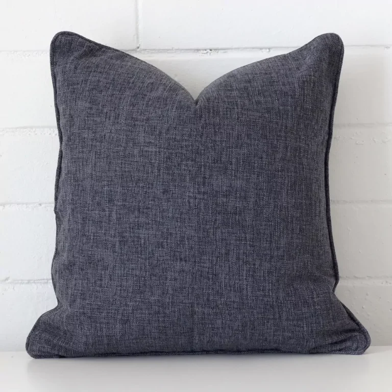 Here a charcoal linen cushion is shown styled against a white wall. It has a square design.