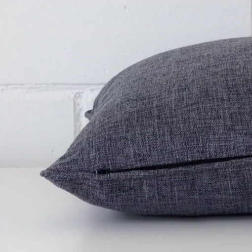 A side shot of a linen cushion cover. The angle shows the edge of the square shape and the charcoal tone.