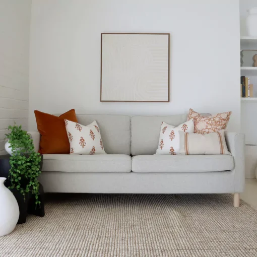 Seven terracotta sofa cushions on a sofa next to a white brick wall.