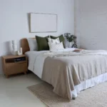 4 olive-coloured bed cushions are next to a green plant in a vase.