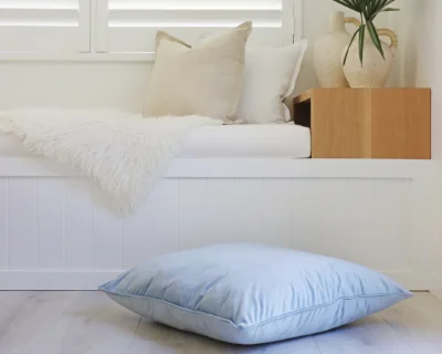 A white bench seat is shown decorated with a blue floor cushion in front of it.