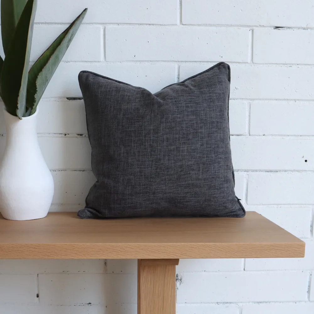 A bench seat with a charcoal cushion and a vase on it.