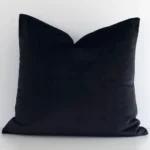 A lovely square black cushion cover arranged in front of a white wall. The solid colour style complements the velvet material.