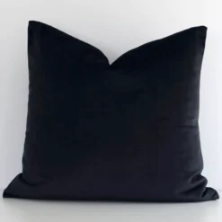 A lovely square black cushion cover arranged in front of a white wall. The solid colour style complements the velvet material.