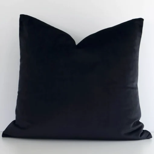 A lovely square black cushion cover arranged in front of a white wall. The solid colour style complements the velvet material.