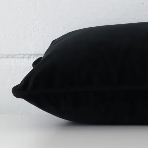 A black cushion arranged sideways in front of a wall. The rectangle size and velvet fabric are shown and the seams are clearly visible.