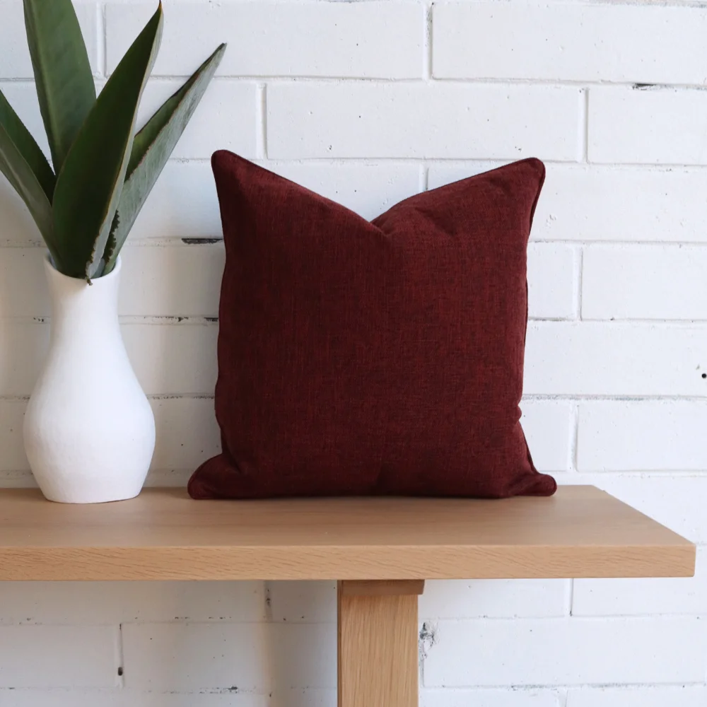 A brick white wall with a burgundy cushion in front of it.
