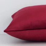 Horizontal edge view of front and back panels of a solid colour velvet cushion in a rectangular shape and with burgundy colouring.