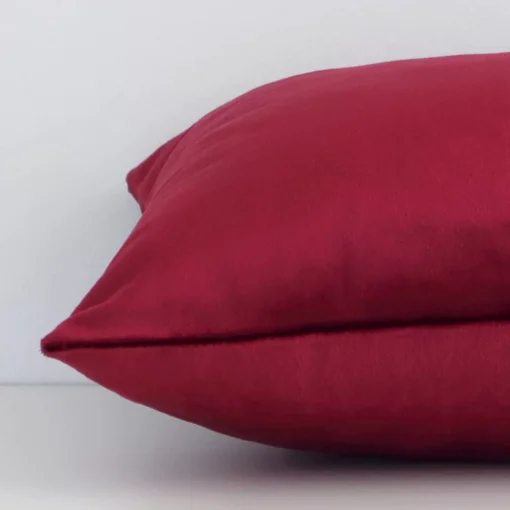 Horizontal edge view of front and back panels of a solid colour velvet cushion in a rectangular shape and with burgundy colouring.