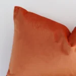 A zoomed in photo of the corner of a burnt solid-coloured cushion that has velvet fabric and a rectangle size.