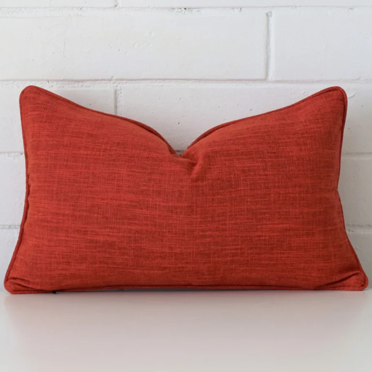 Here a burnt orange linen cushion is shown styled against a white wall. It has a rectangle design.
