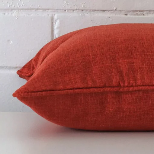 Lateral angle image of a linen square cushion. The burnt orange colour is highlighted.