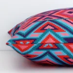 Geometric cushion cover laying sideways against white wall. The square size and outdoor material are shown highlighting the seams.