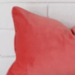 A very close image of the corner of a velvet cushion.The finer detail of the rectangle shape and coral colour are visible.