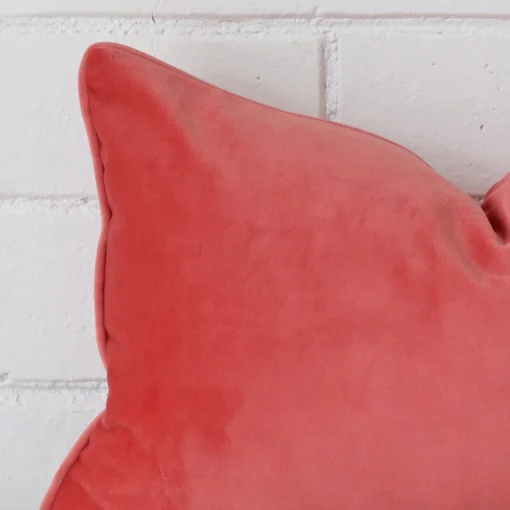 A very close image of the corner of a velvet cushion.The finer detail of the rectangle shape and coral colour are visible.