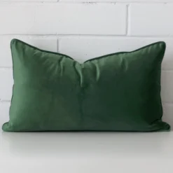 A rectangle cushion in a delightful dark sage tone rests against a white wall. The velvet material appears to be of exceptional quality.