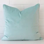 Duck eggcushion positioned in front of a brick wall. It has large dimensions and is made from a velvet material.