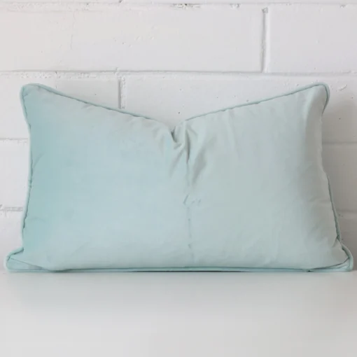 Duck egg cushion leans elegantly against a brick wall. It has been crafted from a high quality velvet material and has a square shape.