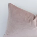 Rectangle solid-coloured cushion in dusty pink colour sitting upright in front of a white wall. It has been made from a quality velvet material.