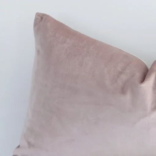 Rectangle solid-coloured cushion in dusty pink colour sitting upright in front of a white wall. It has been made from a quality velvet material.