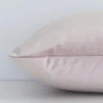 Dusty pink solid colour cushion cover laying sideways against white wall. The rectangle size and velvet material are shown highlighting the seams.