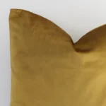 A macro image of the top left corner of this solid-coloured velvet cushion. It is possible to see the finer detail of the square shape and gold mustard colour.
