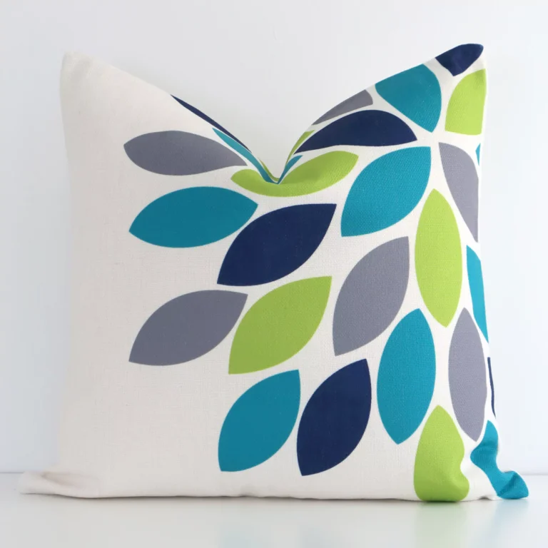 White wall with a patterned colourful cushion laying against it. It has a distinctive linen fabric and has a square shape.