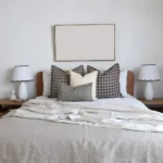 A set of 4 designer bed cushions on a wooden bed between two white lampshades.