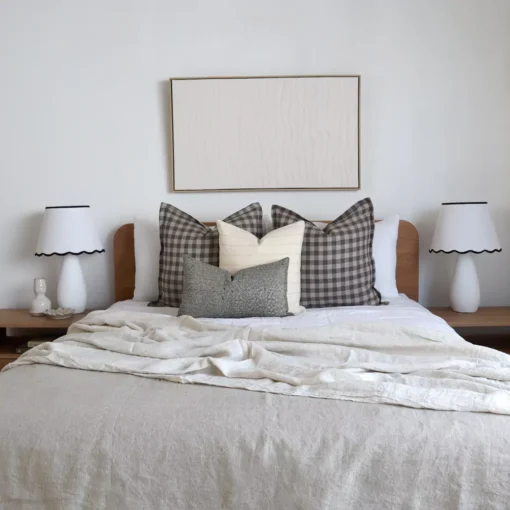 A set of 4 designer bed cushions on a wooden bed between two white lampshades.