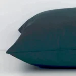 Pine green cushion laid horizontally. This perspective shows the edge of the outdoor fabric and its square shape.