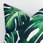 Close up image of outdoor square cushion. The image allows you to see the green hue and tropical leaf print more thoroughly.