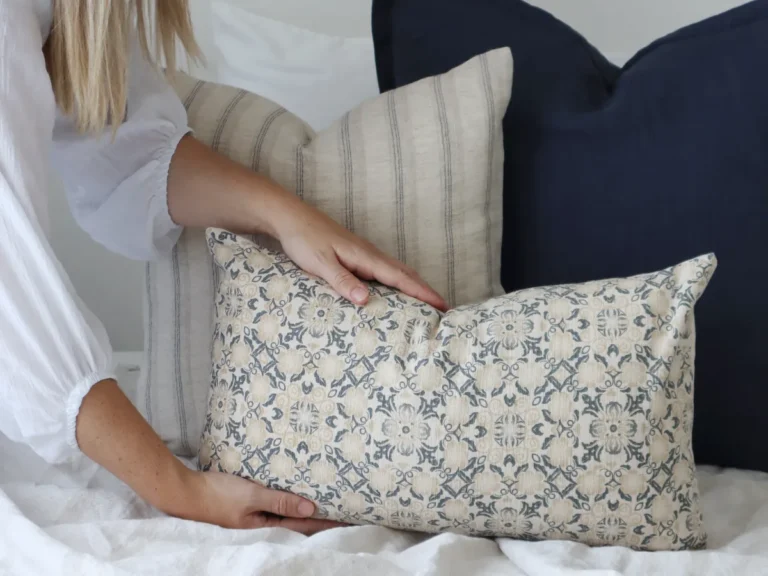A lady is arranging cushions and is about to place a cushion in front of the collection.
