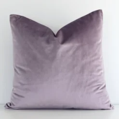 Lavender solid-coloured cushion cover in front of a white wall. It is square-shaped and is made from a velvet material.