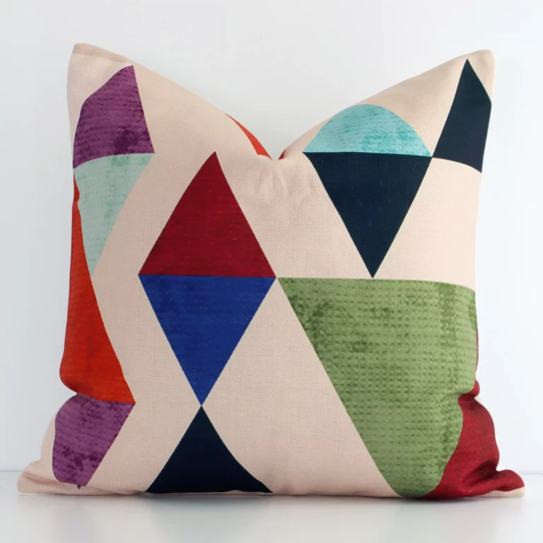 A linen square cushion with a vibrant geometric design positioned upright against a white wall. The cushion features a mix of colourful prints.