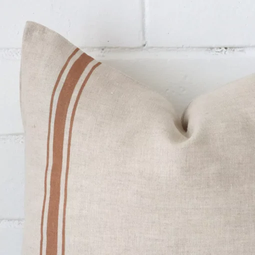 A linen square cushion’s corner has been enlarged in this shot. The detail of the striped design and terracotta colour are visible.