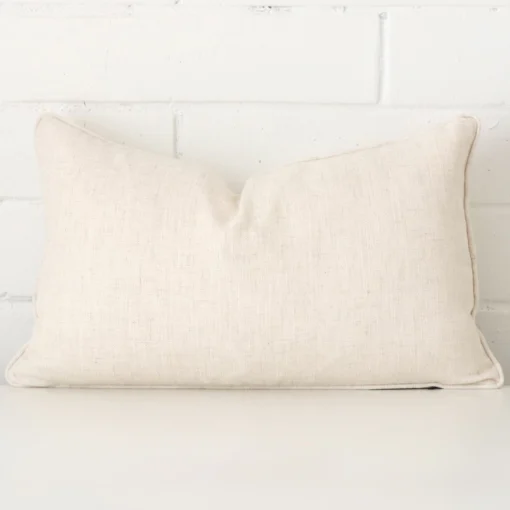 A brick wall that has a cream cushion cover positioned in front of it. It has an exquisite linen material and a lovely rectangle shape.