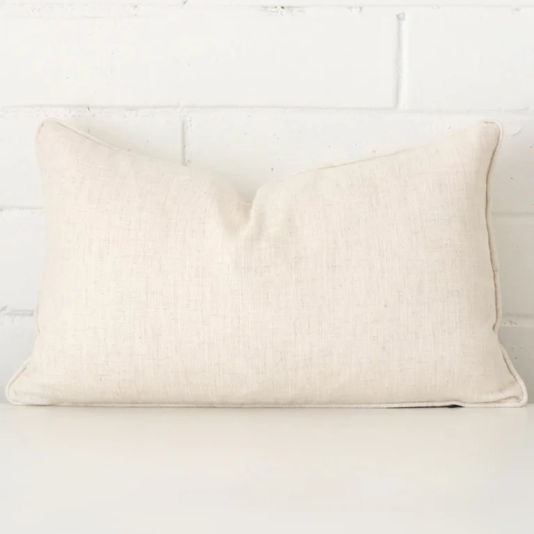 A brick wall that has a cream cushion cover positioned in front of it. It has an exquisite linen material and a lovely rectangle shape.