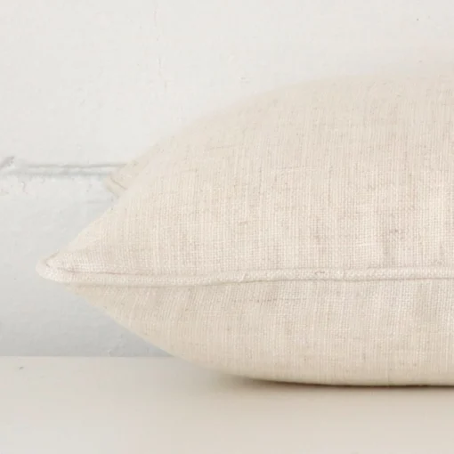 A linen cream cushion cover shown laying on its side. The edge of its rectangle size is shown.